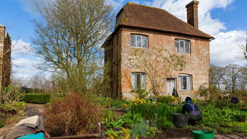 Gardener at work, kneeling in a flowerbed in the South Cottage garden at Sissinghurst Castle Garden, Kent